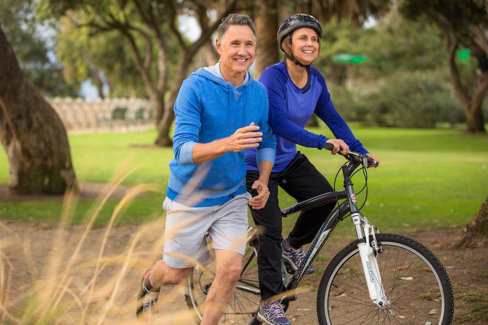 A man jogging and a woman biking outdoors on a sunny day