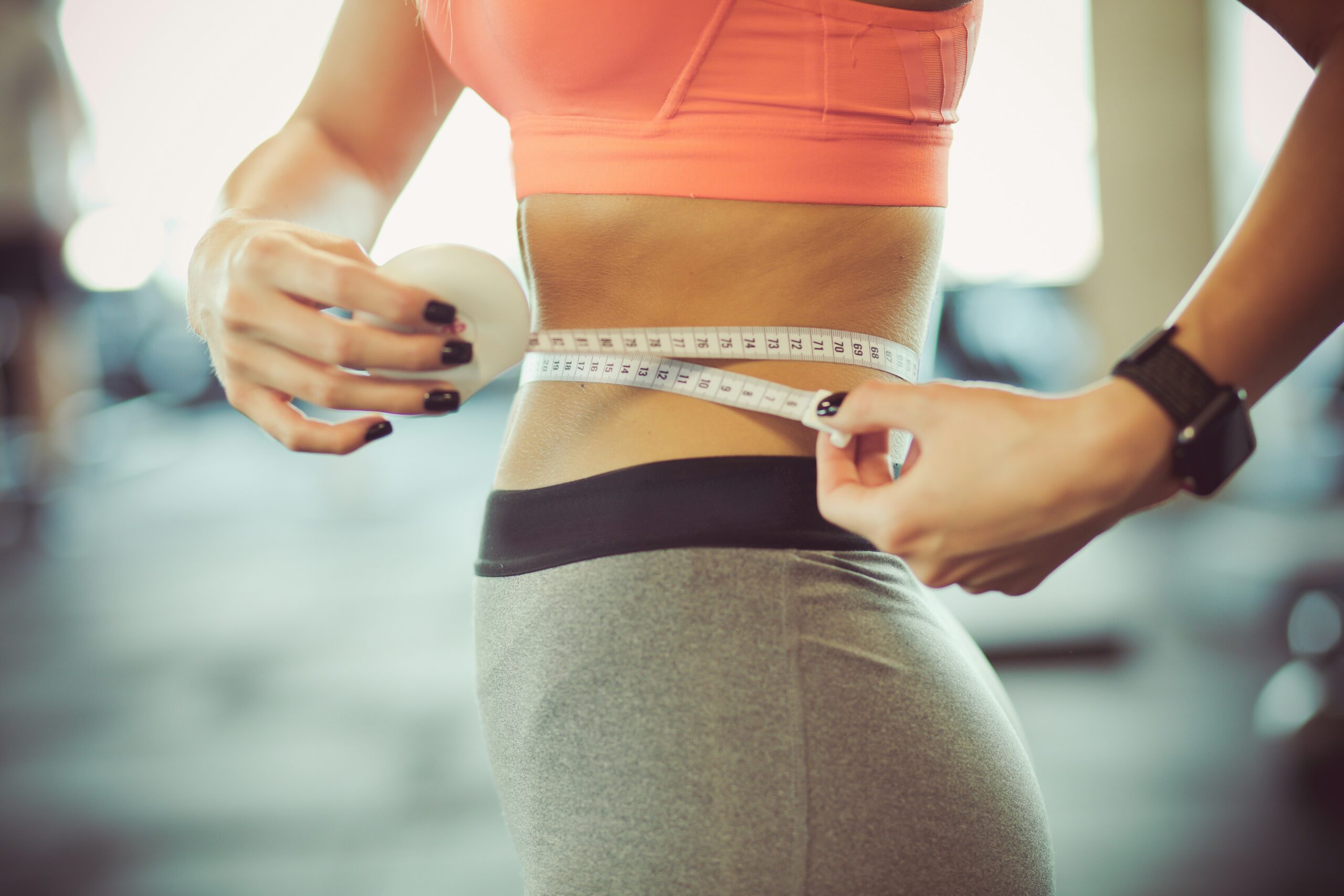 A woman measuring her waist with a tape measure, representing progress in a GLP-1 weight loss program.
